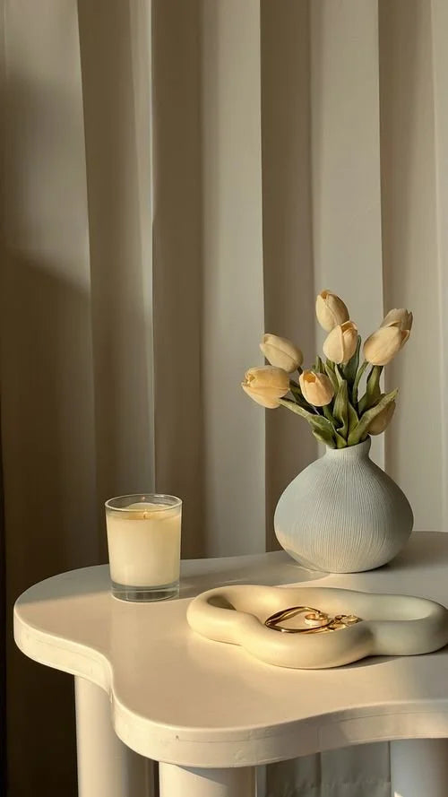A vase of cream tulips and a candle on a curved white side table
