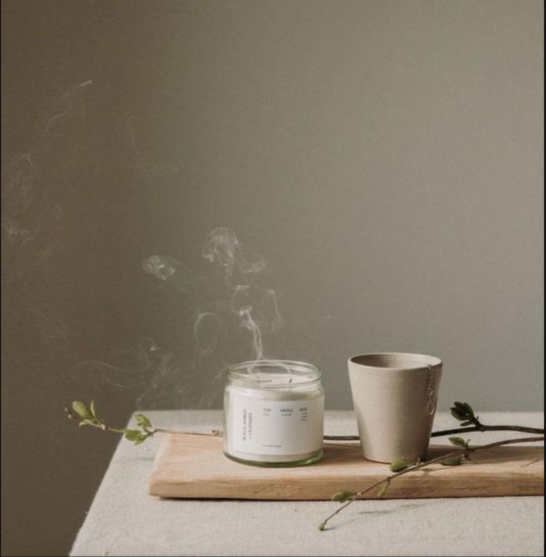 A lit candle and a ceramic cup on a wooden tray