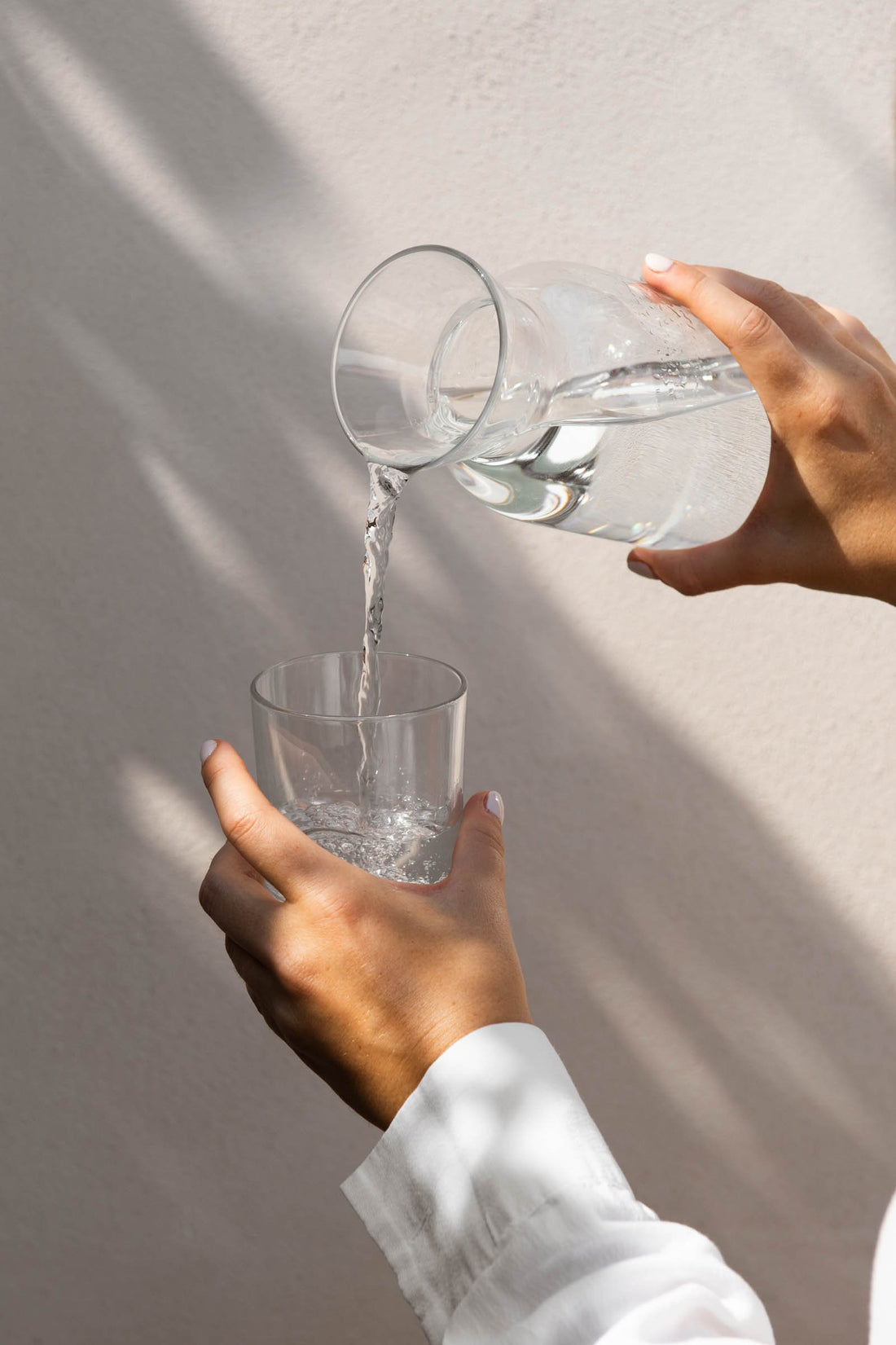 A hand pouring water from a glass carafe into a glass