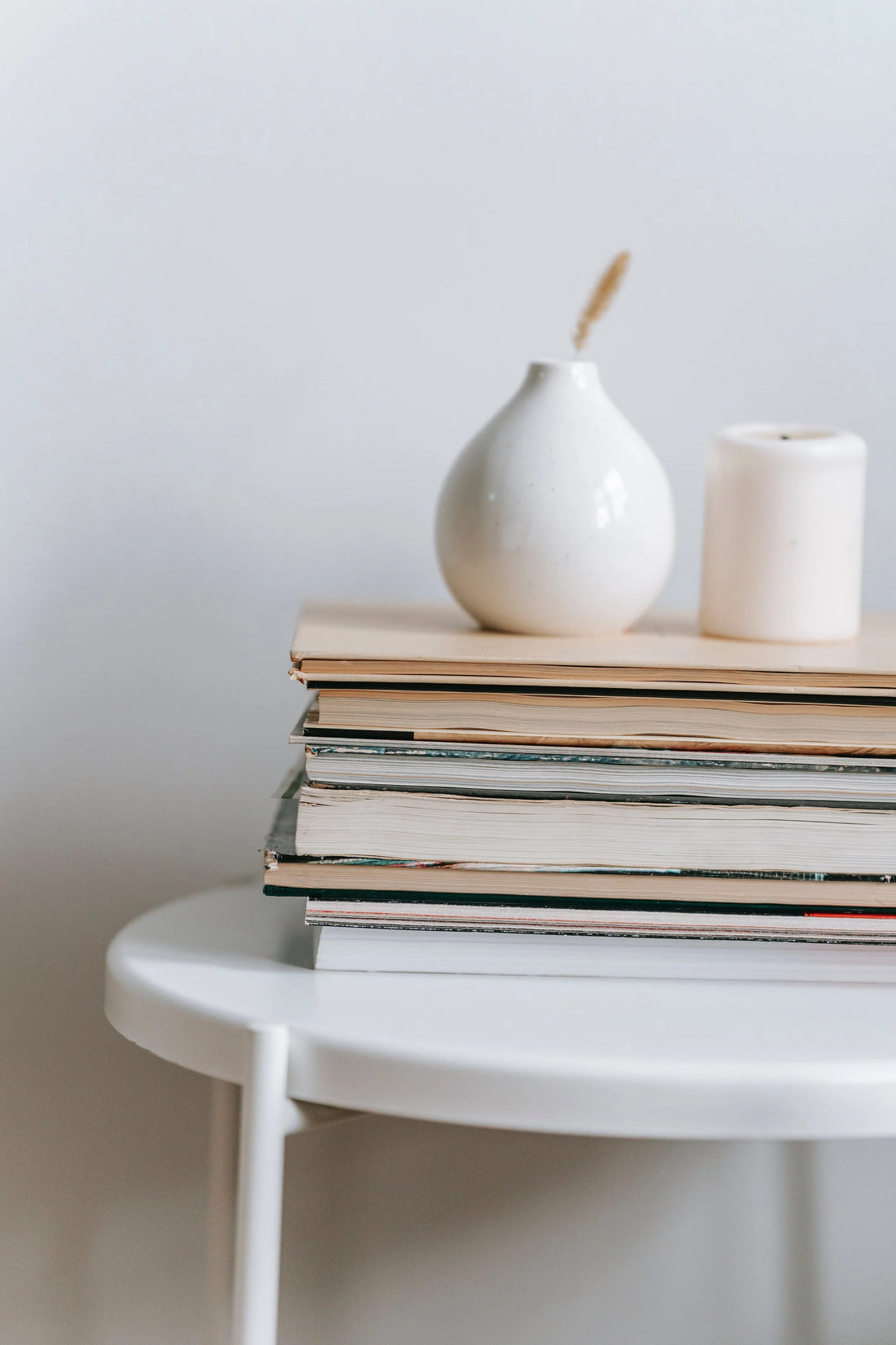 A stack of books with a white vase and candle on a round side table