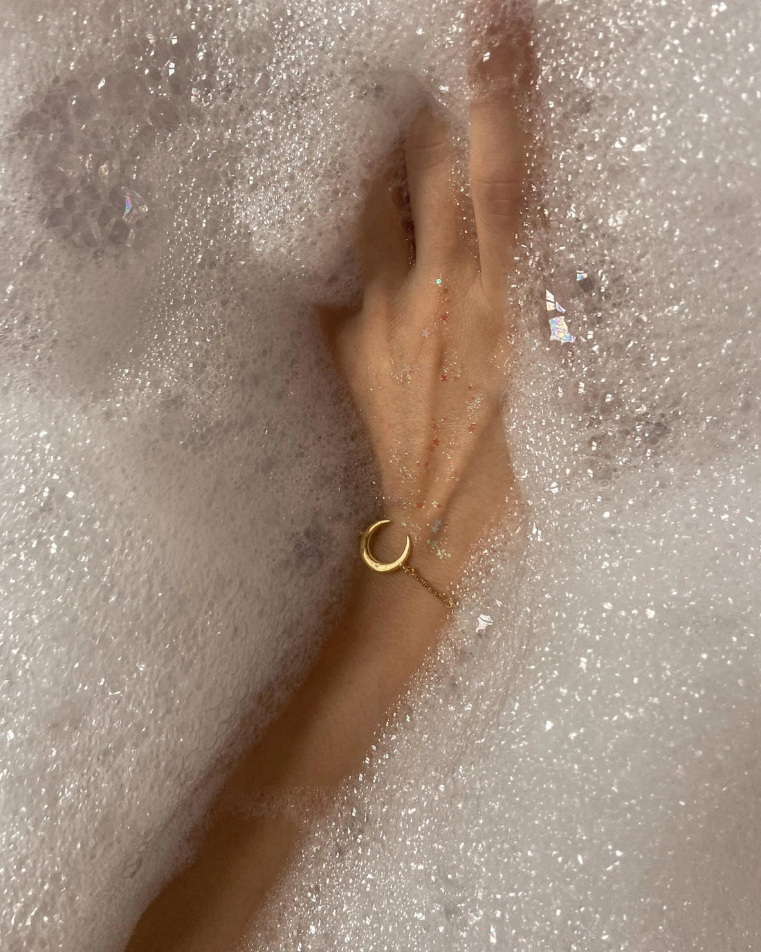 A hand with a gold ring resting in bath foam