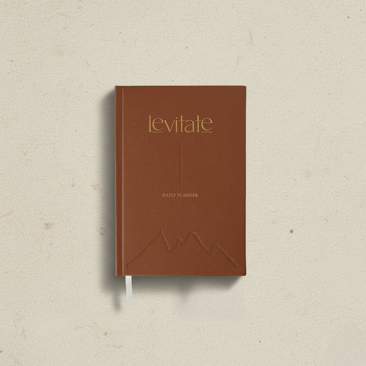 The Levitate Daily Planner in cognac brown, gold foil wordmark, embossed mountain and ribbon marker